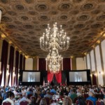 A large crowd looks on to a decadent set & stage design at a corporate meeting